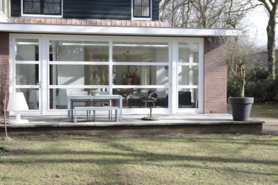 Woninguitbreiding met grote glazen pui die een panoramisch uitzicht op de tuin biedt.