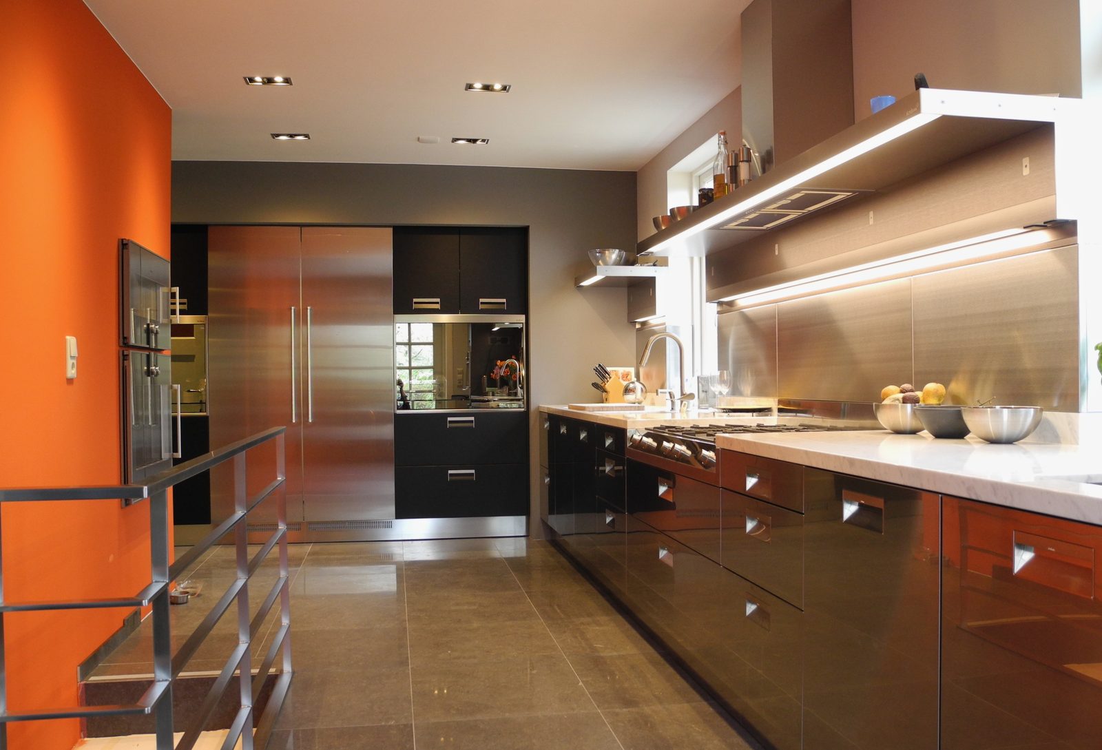 Luxe Arclinea keuken met RVS elementen, donker eiken kasten en een opvallende oranje wand.