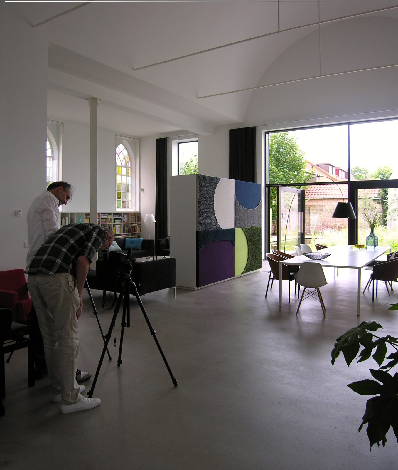 Fotografen maken opnames van een modern interieur met een kleurrijk akoestisch paneel in een lichte woonruimte.
