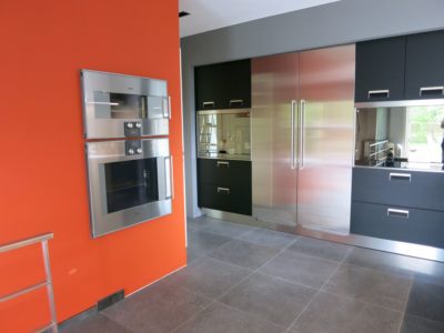 Luxe Arclinea keuken met RVS apparatuur, donker eiken kasten en een opvallende oranje accentmuur.