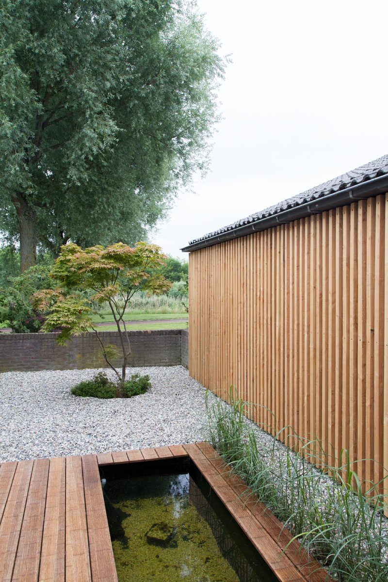 Moderne tuin met houten vlonder, vijver en een gevel bekleed met verticale houten latten.