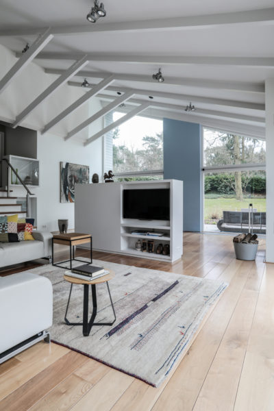 Lichte woonkamer met op maat gemaakt tv-meubel, houten vloer en zicht op de tuin in een moderne villa.