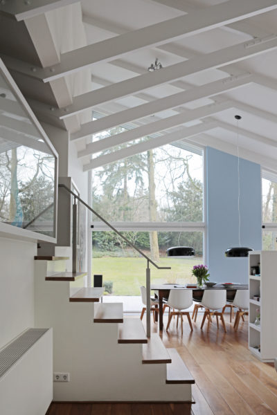 Licht interieur van een villa met open trap, houten vloer en zicht op de tuin vanuit de eetkamer.