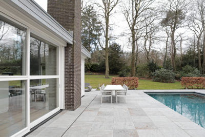 Luxe villa-terras met zwembad, strakke eettafel en zicht op de moderne keuken door de glazen pui.