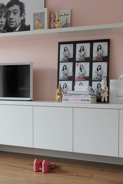 Strak wit zwevend dressoir tegen een zachtroze wand met decoratieve kunst en boeken in een modern interieur.