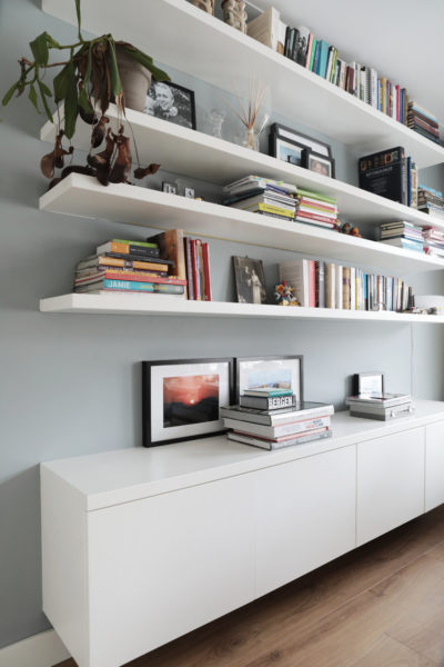 Strak wit maatwerk dressoir met daarboven zwevende boekenplanken tegen een lichtgrijze wand.