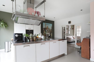 Moderne witte keuken met RVS werkblad en hangende afzuigkap in een sfeervol interieur.