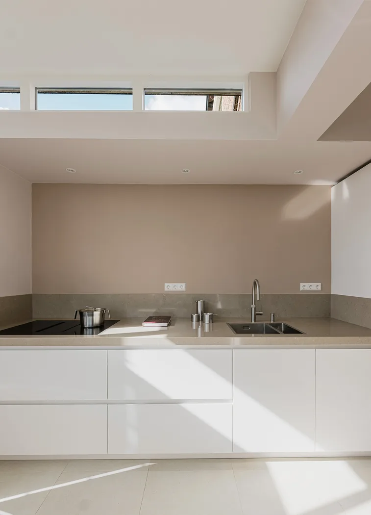 Strakke witte Cesar Maxima 2.2 keuken met minimalistisch aanrechtblad en lichtinval via bovenlicht.