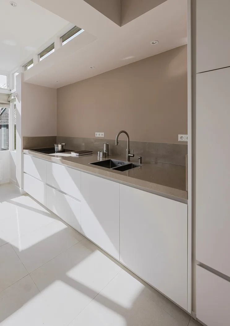 Strakke, minimalistische Cesar Maxima 2.2 keuken met wit front en een beige werkblad in een lichte ruimte.
