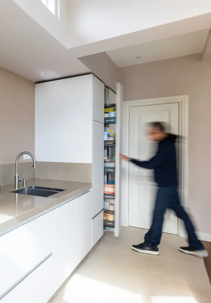 Persoon opent de efficiënte uittrekbare voorraadkast in een strakke witte Cesar Maxima 2.2 keuken.