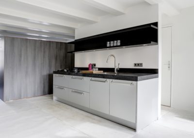 Strakke aluminium keuken met zwart werkblad en wandplank in een modern Amsterdams appartement.