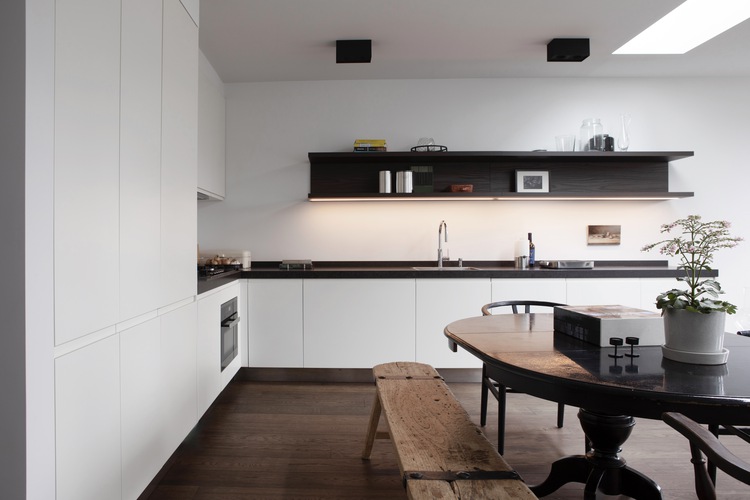 Moderne witte keuken met donkerhouten werkblad, wandplanken en eethoek in een vernieuwde woonruimte.