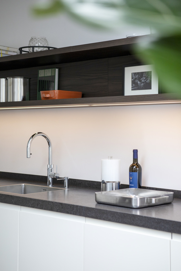 Strak keukenblad met spoelbak en verlichte wandplank in een modern interieur.
