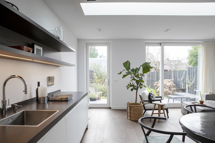 Strakke keuken met donker werkblad en open wandplanken in een licht vernieuwd interieur met zicht op de tuin.