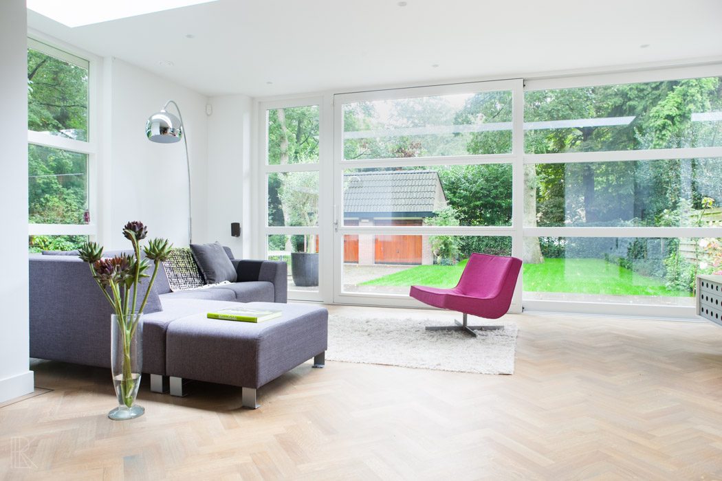 Lichte woonkameruitbreiding met visgraatvloer, moderne meubels en panoramisch uitzicht op de tuin.